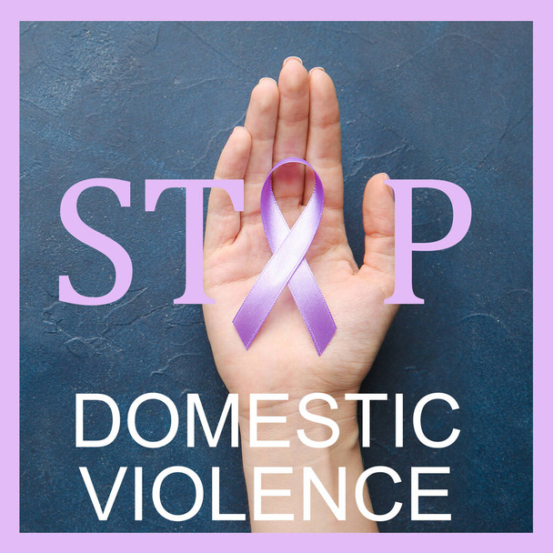 Női kéz lila szalaggal és szöveggel STOP DOMESTIC VIOLENCE színes háttér - Fotó, kép