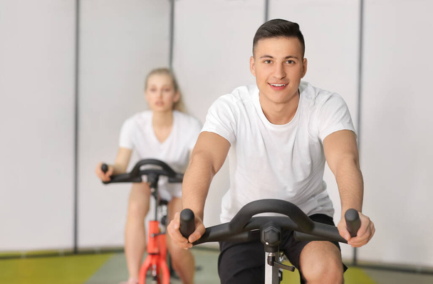 Young man training on exercising bike in gym - Valokuva, kuva