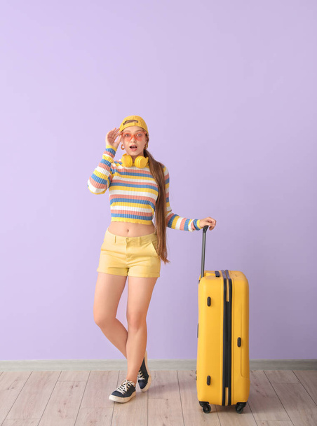 Έκπληκτη νεαρή γυναίκα με βαλίτσα κοντά σε χρωματιστό τοίχο. Ταξιδιωτική έννοια - Φωτογραφία, εικόνα