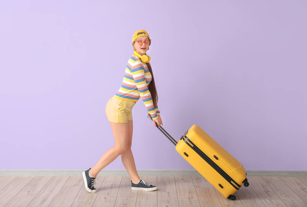 カラーウォールの近くにスーツケースを着た若い女性。旅行のコンセプト - 写真・画像