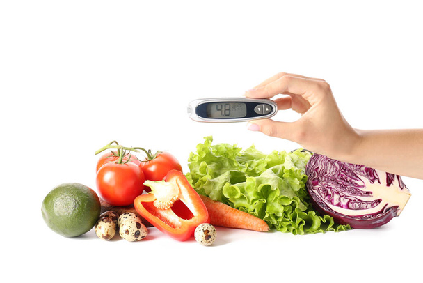 Naiskäsi glukometrillä ja vihanneksilla valkoisella taustalla. Diabetes-käsite - Valokuva, kuva