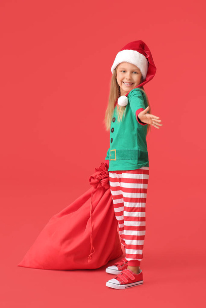 Cute little girl dressed as elf and with Santa Claus bag on color background - Foto, imagen