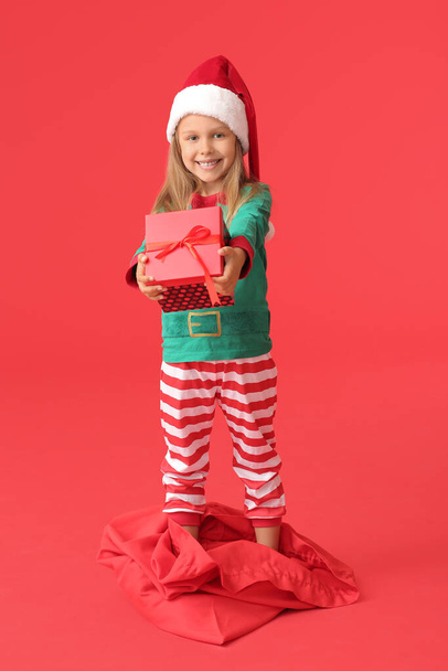 Cute little girl dressed as elf and with Christmas gift on color background - Foto, afbeelding