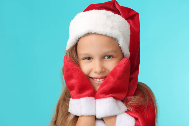 Nettes kleines Mädchen im Weihnachtsmannkostüm auf farbigem Hintergrund - Foto, Bild