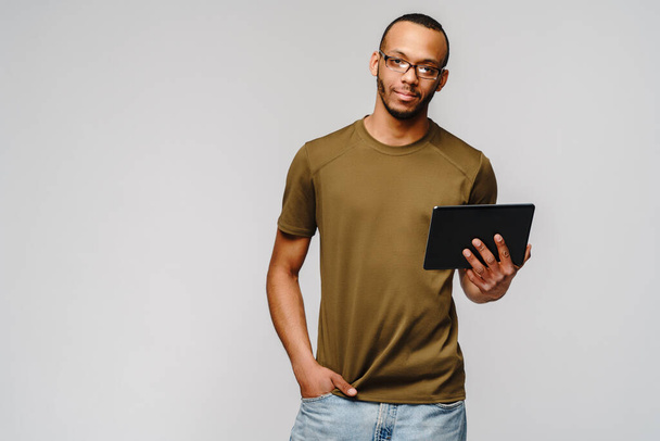 Portrait of a young african american man wearing green t-shirt holding tablet pc pad - 写真・画像