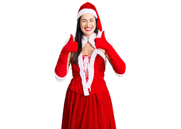 Nuori kaunis valkoihoinen nainen yllään joulupukki puku menestyksen merkki tekee positiivisen eleen käsin, peukalot ylös hymyillen ja onnellinen. iloinen ilme ja voittaja ele.  - Valokuva, kuva