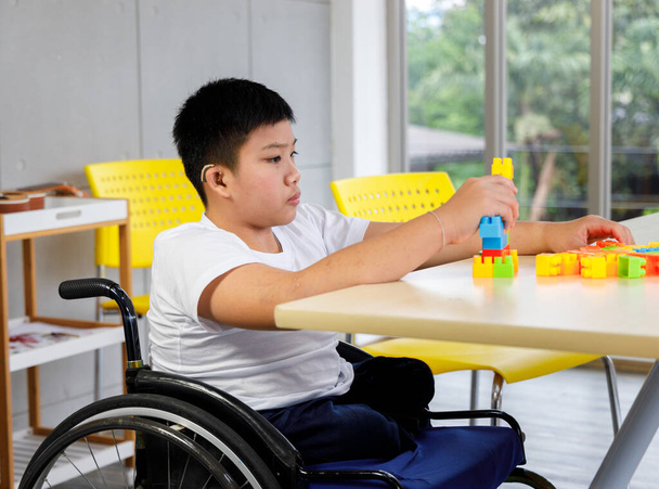 車椅子の障害児は教室でカラフルなパズルおもちゃをプレイします。学校で学ぶ障害児の概念. - 写真・画像