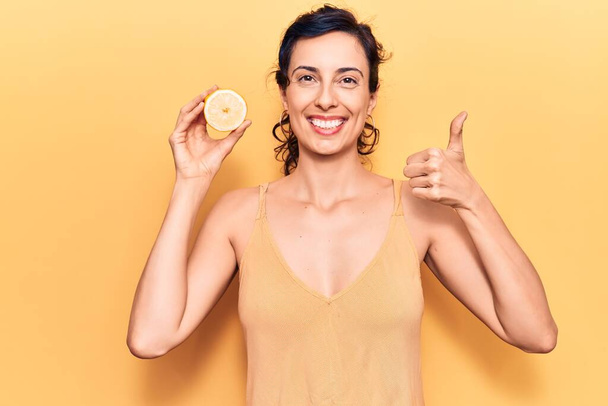 Молода красива іспаномовна жінка тримає лимон усміхнений щасливий і позитивний, великий палець робить відмінний знак схвалення
  - Фото, зображення