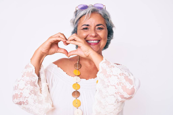 Ältere hispanische grauhaarige Frau in lässiger Hippie-Kleidung, die verliebt lächelt und Herzsymbole mit den Händen formt. Romantisches Konzept.  - Foto, Bild