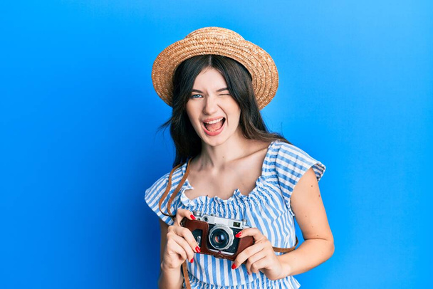 Νεαρό όμορφο καυκάσιο κορίτσι κρατώντας vintage κάμερα κλείνει το μάτι κοιτάζοντας την κάμερα με σέξι έκφραση, χαρούμενο και χαρούμενο πρόσωπο.  - Φωτογραφία, εικόνα