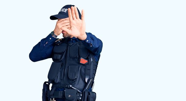 Mladý pohledný muž v policejní uniformě, zakrývající oči rukama a zastavující gesto se smutným a ustrašeným výrazem. trapný a negativní koncept.  - Fotografie, Obrázek