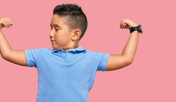 腕の筋肉を示すカジュアルな服を着ている小さな男の子のヒスパニック系の子供は誇りに思って笑う。フィットネスのコンセプト.  - 写真・画像