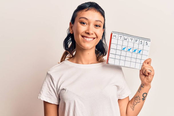 Νεαρή γυναίκα κρατώντας ημερολόγιο ταξιδιού αναζητούν θετική και ευτυχισμένη στέκεται και χαμογελά με αυτοπεποίθηση χαμόγελο που δείχνει τα δόντια  - Φωτογραφία, εικόνα