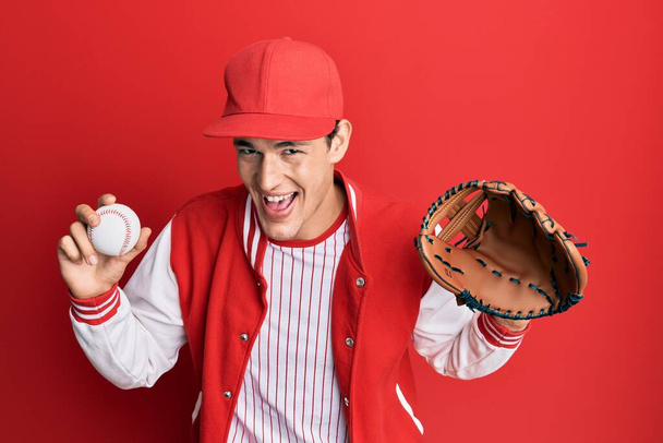 Handsome caucasian man wearing baseball uniform holding golve and ball smiling and laughing hard out loud because funny crazy joke.  - Foto, Bild
