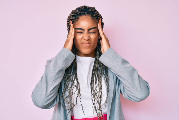 Junge afrikanisch-amerikanische Frau mit Zöpfen in Businessjacke leidet unter Kopfschmerzen verzweifelt und gestresst, weil Schmerzen und Migräne. Hände auf den Kopf.  - Foto, Bild