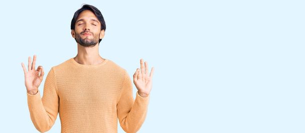 Handsome hispanic man wearing casual sweater relax and smiling with eyes closed doing meditation gesture with fingers. yoga concept.  - Photo, Image
