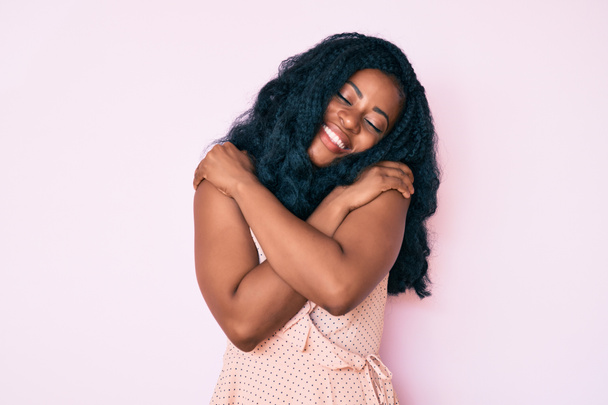 Beautiful african woman wearing casual summer clothes hugging oneself happy and positive, smiling confident. self love and self care  - Photo, Image