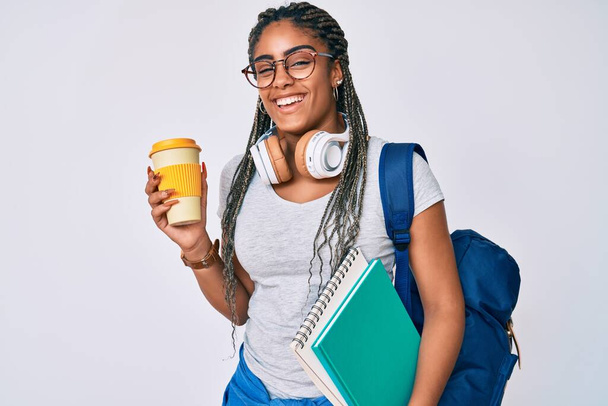 Jovem afro-americana com tranças usando mochila estudantil bebendo café sorrindo e rindo em voz alta porque piada louca engraçada.  - Foto, Imagem