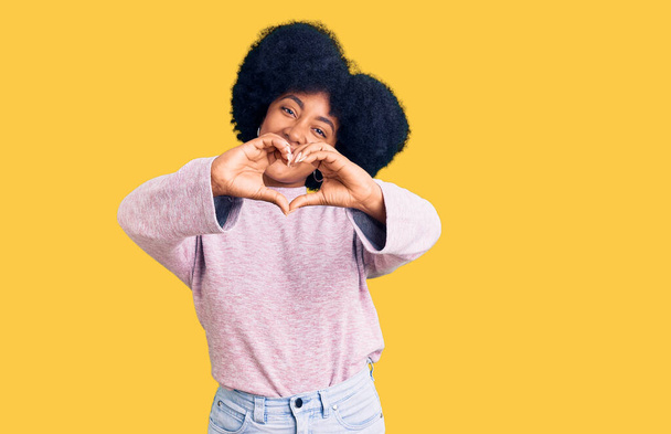 Joven chica afroamericana vistiendo ropa casual sonriendo en el amor haciendo forma de símbolo del corazón con las manos. concepto romántico.  - Foto, Imagen