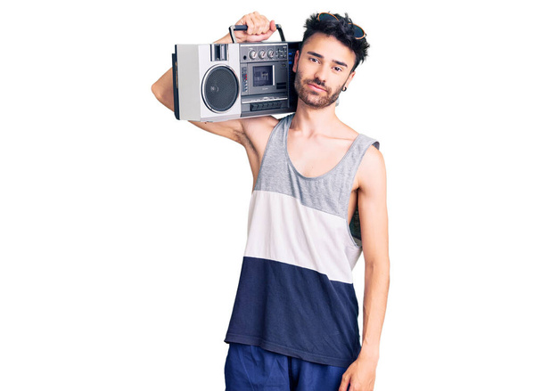 Jonge Spaanse man met boombox, luisteren naar muziek denken houding en nuchtere uitdrukking op zoek naar zelfvertrouwen  - Foto, afbeelding