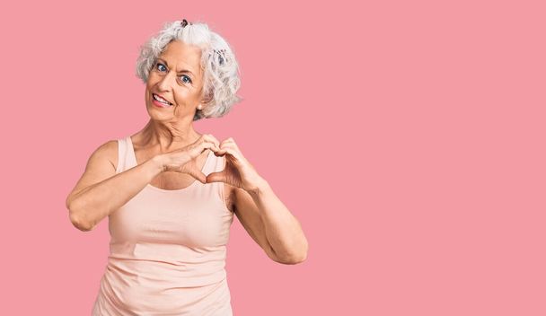Senior grijs-harige vrouw draagt casual kleding glimlachend in liefde tonen hart symbool en vorm met de handen. romantisch concept.  - Foto, afbeelding