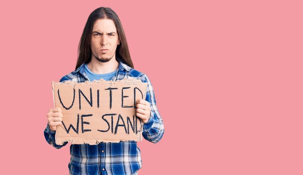 Νεαρός ενήλικος άνδρας με μακριά μαλλιά κρατώντας ενωμένη στεκόμαστε banner σκέψης στάση και νηφάλια έκφραση αναζητούν αυτοπεποίθηση  - Φωτογραφία, εικόνα
