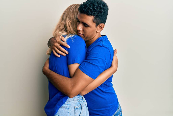 Jovem casal interracial vestindo roupas casuais abraçando-se feliz e positivo, sorrindo confiante. auto-amor e auto-cuidado  - Foto, Imagem