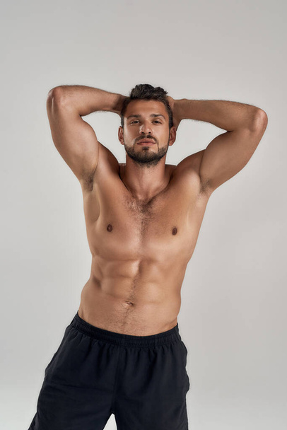 Young muscular caucasian man looking at camera and showing his naked torso while posing shirtless isolated over grey background - Fotoğraf, Görsel
