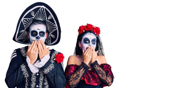 Young couple wearing mexican day of the dead costume over background laughing and embarrassed giggle covering mouth with hands, gossip and scandal concept  - Photo, Image
