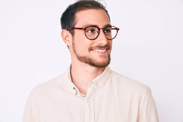 Young handsome man wearing casual clothes and glasses looking away to side with smile on face, natural expression. laughing confident.  - Fotoğraf, Görsel