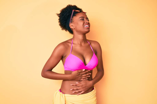 Giovane donna afroamericana in bikini con la mano sullo stomaco perché nausea, malattia dolorosa sensazione di malessere. concetto di dolore.  - Foto, immagini