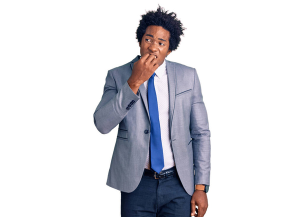 Schöner afrikanisch-amerikanischer Mann mit Afrohaaren, der eine Businessjacke trägt und gestresst und nervös aussieht, die Hände auf den Mund beißenden Nägeln. Angstproblem.  - Foto, Bild
