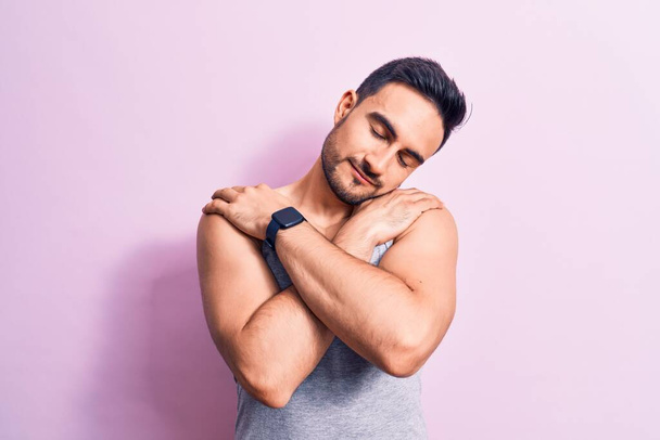 Young handsome man with beard wearing casual sleeveless t-shirt over pink background hugging oneself happy and positive, smiling confident. Self love and self care - Photo, Image