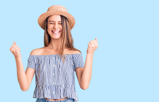 Young beautiful girl wearing hat and t shirt excited for success with arms raised and eyes closed celebrating victory smiling. winner concept.  - Fotoğraf, Görsel