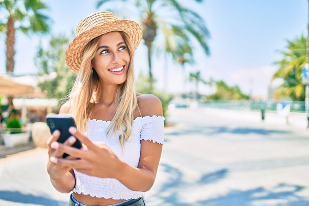 Junge blonde Touristin lächelt glücklich mit Smartphone in die Stadt. - Foto, Bild