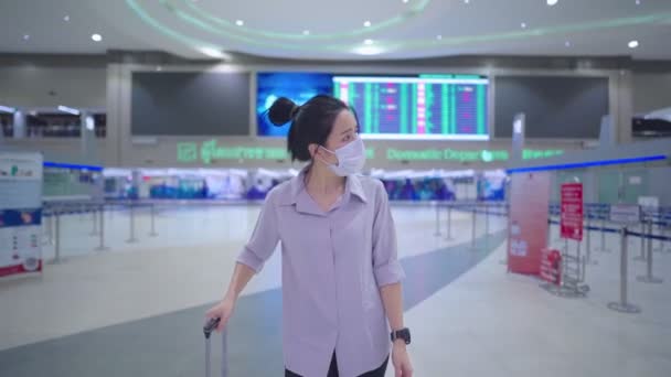 Asiatique Jeune femme porter masque facial marche avec chariot à bagages de voyage dans le couloir terminal de l'aéroport, comptoir d'enregistrement, départ arrivée voyage pick up, heure d'embarquement, pandémie de transport en commun - Séquence, vidéo