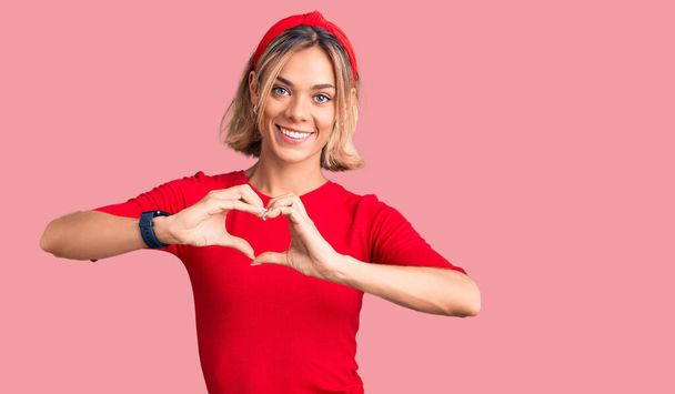 Beautiful caucasian woman wearing casual clothes and red diadem smiling in love showing heart symbol and shape with hands. romantic concept.  - Photo, Image