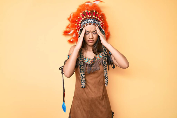 Young beautiful latin girl wearing indian costume with hand on head, headache because stress. suffering migraine.  - Photo, image