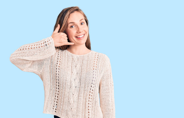 Young beautiful blonde woman wearing casual sweater smiling doing phone gesture with hand and fingers like talking on the telephone. communicating concepts.  - Photo, Image
