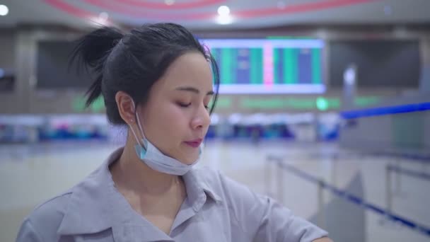 Jonge vrouw draagt gezichtsmasker in luchthaven, in lege luchthaventerminal Tijdtafel groot scherm, Risico van reizen tijdens covid-19 pandemie, nieuwe normale sociale afstand, Ziektepreventie overbrengen - Video