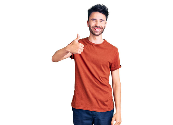 Fiatal spanyol férfi alkalmi ruhát visel mosolygós boldog és pozitív, hüvelykujj fel csinál kiváló és jóváhagyási jel  - Fotó, kép