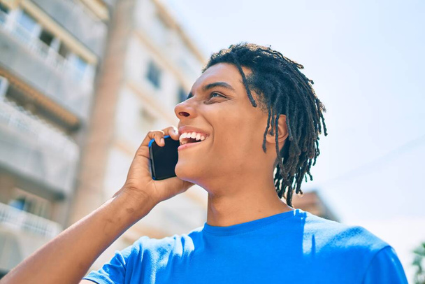 Genç Afrikalı Amerikalı gülümseyen mutlu bir adam şehrin caddesinde akıllı telefondan konuşuyor.. - Fotoğraf, Görsel