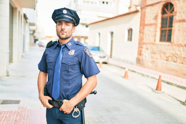 Młody, przystojny policjant w mundurze policyjnym. Stojąc z poważnym wyrazem twarzy na ulicy miasta. - Zdjęcie, obraz