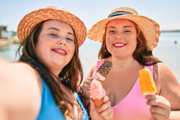 Dvě plus velikost nadváha sestry dvojčata ženy jíst sladkou zmrzlinu na pláži o letních prázdninách - Fotografie, Obrázek