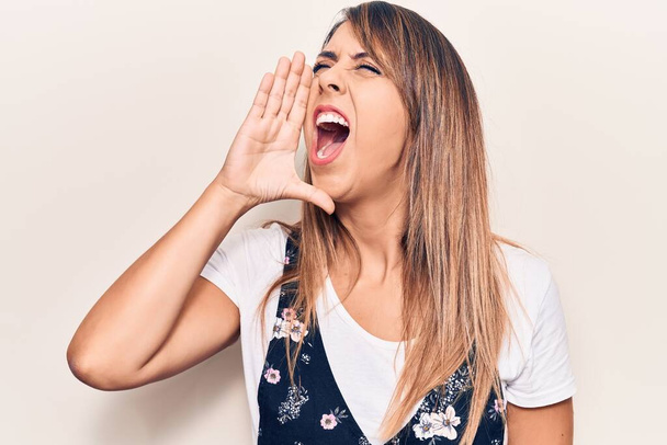 Young beautiful woman wearing casual floral dress shouting and screaming loud to side with hand on mouth. communication concept.  - Photo, Image