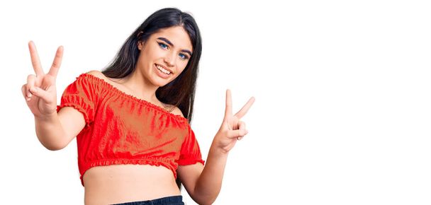 Brunette teenager girl wearing casual clothes smiling looking to the camera showing fingers doing victory sign. number two.  - Photo, Image