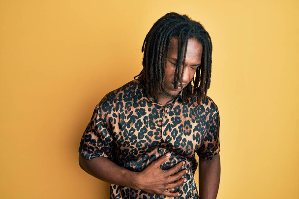 Afrikanischer Mann mit Zöpfen in Leoparden-Animal-Print-Shirt mit der Hand auf dem Bauch, weil Verdauungsstörungen, schmerzhafte Krankheit fühlen sich unwohl. Schmerzkonzept.  - Foto, Bild