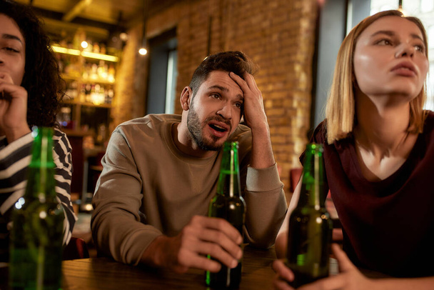 Close up of friends looking disappointed while watching sports match on TV together, drinking beer and cheering for team in the bar. People, leisure, friendship and entertainment concept - Фото, изображение