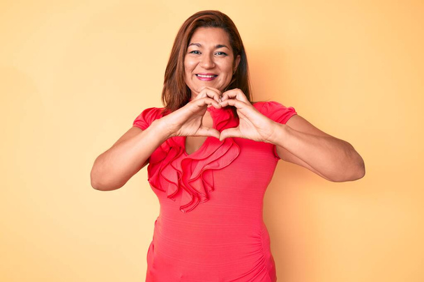 Middle age brunette hispanic woman wearing summer dress smiling in love showing heart symbol and shape with hands. romantic concept.  - Photo, Image
