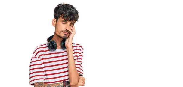 Joven hispano escuchando música usando auriculares pensando que se ve cansado y aburrido con problemas de depresión con los brazos cruzados.  - Foto, imagen